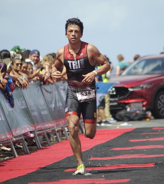 A male triathlete running in a race with spectators in the background.